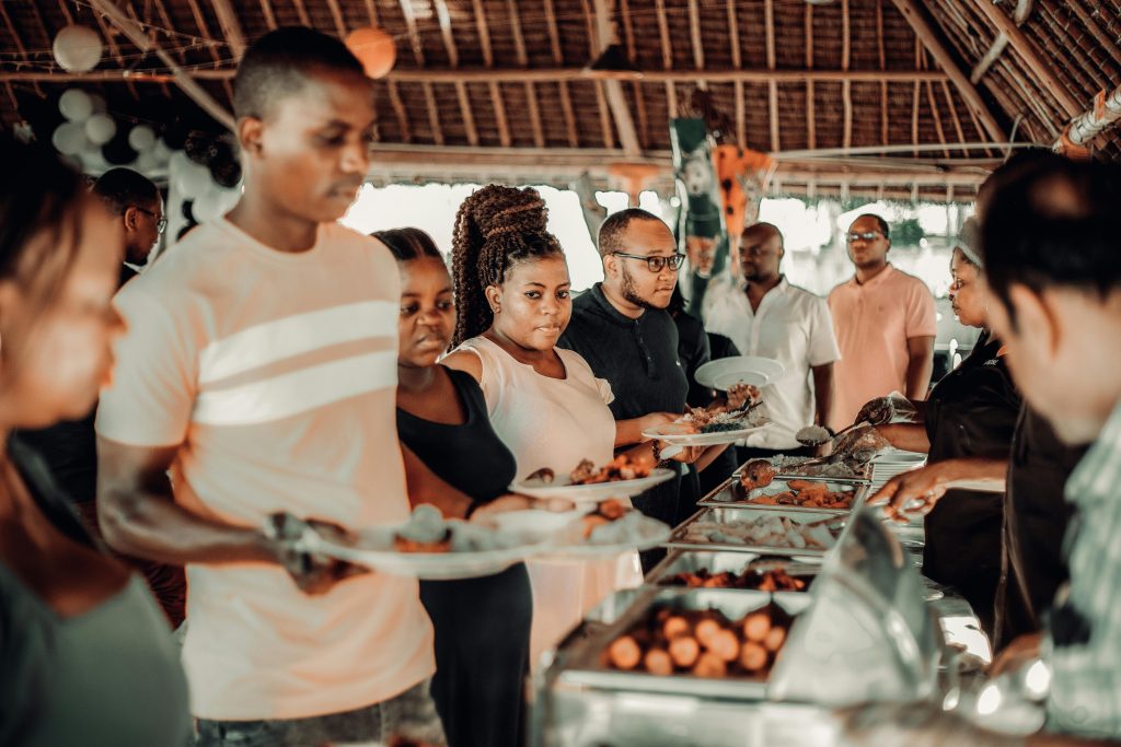 Programmes Group of African adults enjoying a festive buffet indoors with a lively atmosphere.