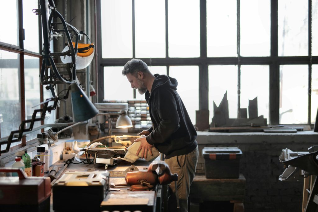 Programmes Side view of male workshop owner standing near messy workbench and fixing metal details while using instruments during work