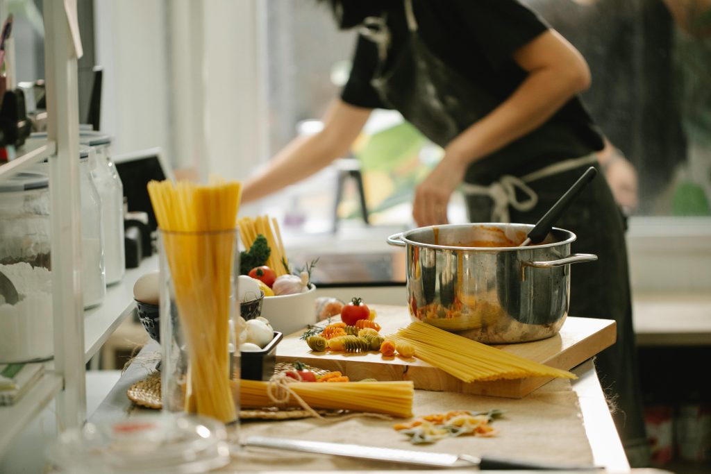Programmes Side view crop anonymous female in apron cooking spaghetti in modern light kitchen