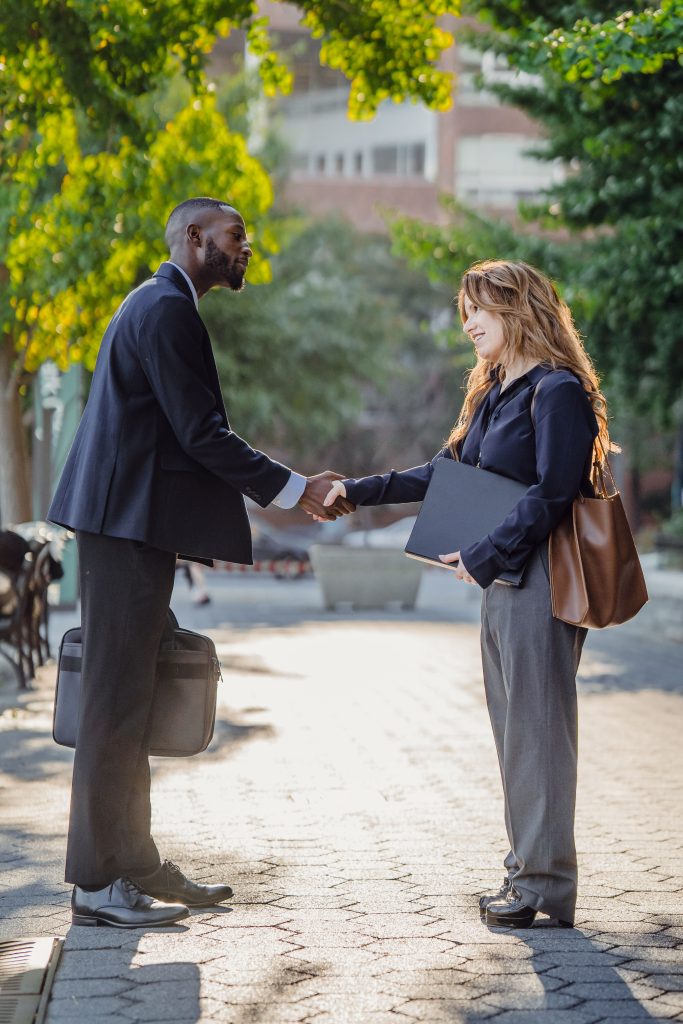 Two professionals exchange a handshake in a sunlit urban setting, symbolizing agreement and partnership.