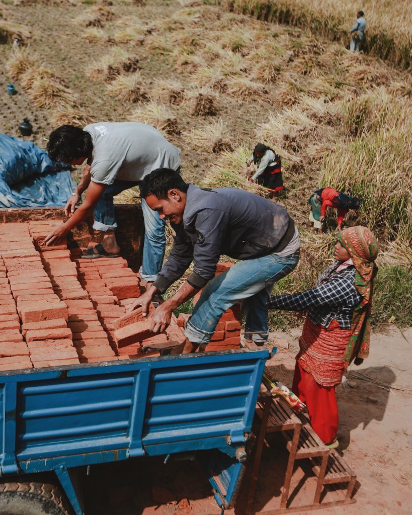 Rural workers loading stacks of bricks onto a truck in a countryside field.