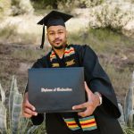 African American graduate joyfully displays diploma in outdoor ceremony.