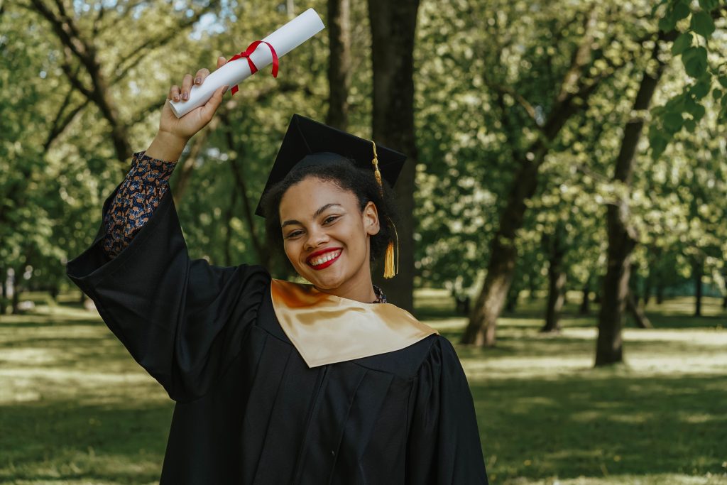 Home Happy graduate celebrating outdoors, holding diploma with a smile.
