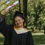 Happy graduate celebrating outdoors, holding diploma with a smile.
