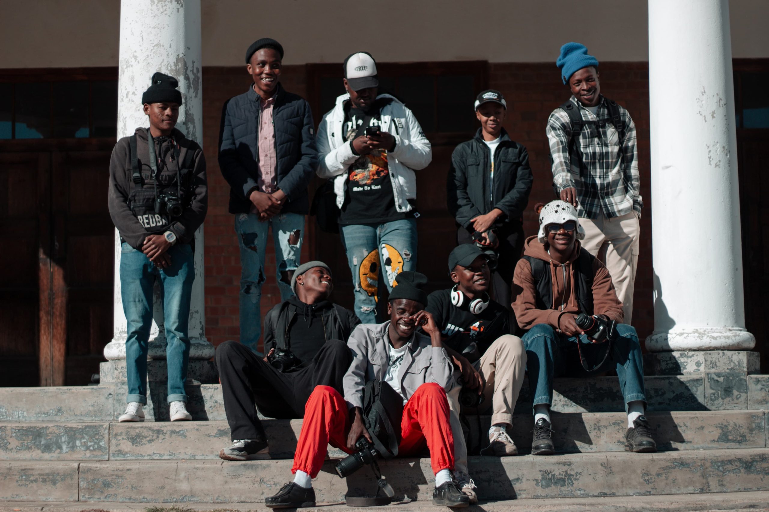 A group of young adults sitting and standing together on steps outdoors in Winburg, South Africa, showcasing street style fashion.
